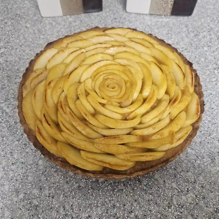 A close-up photo of a baked apple tart with thinly sliced apples arranged in a spiral pattern resembling a rose, sitting on…