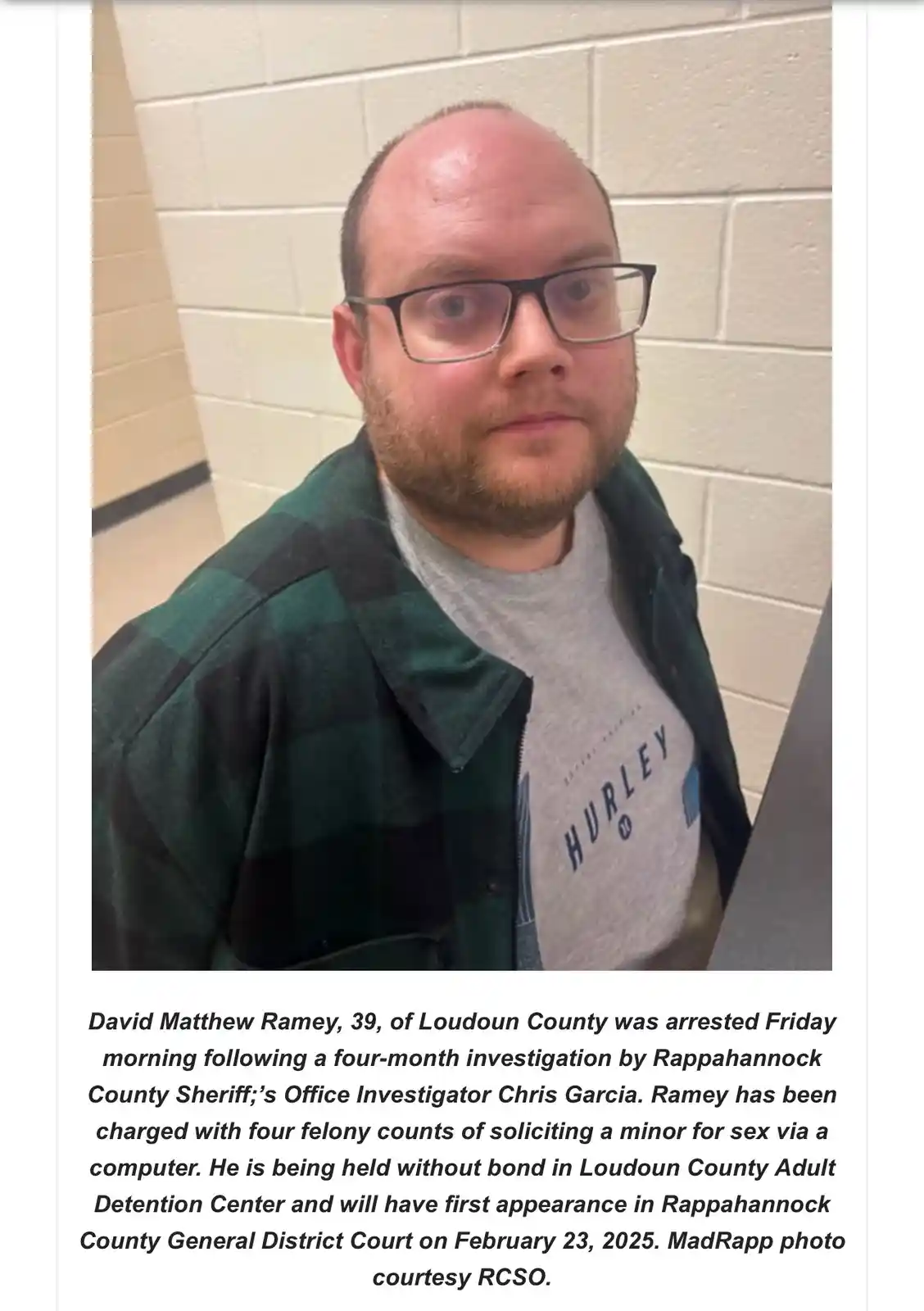 A mugshot-style photo shows a man with glasses and a beard wearing a green plaid shirt over a grey Hurley t-shirt, standing…