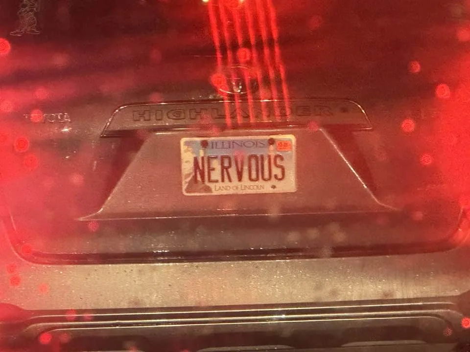 A close-up photo of the rear of a Toyota Highlander, showing an Illinois license plate with the word 'NERVOUS' printed on…