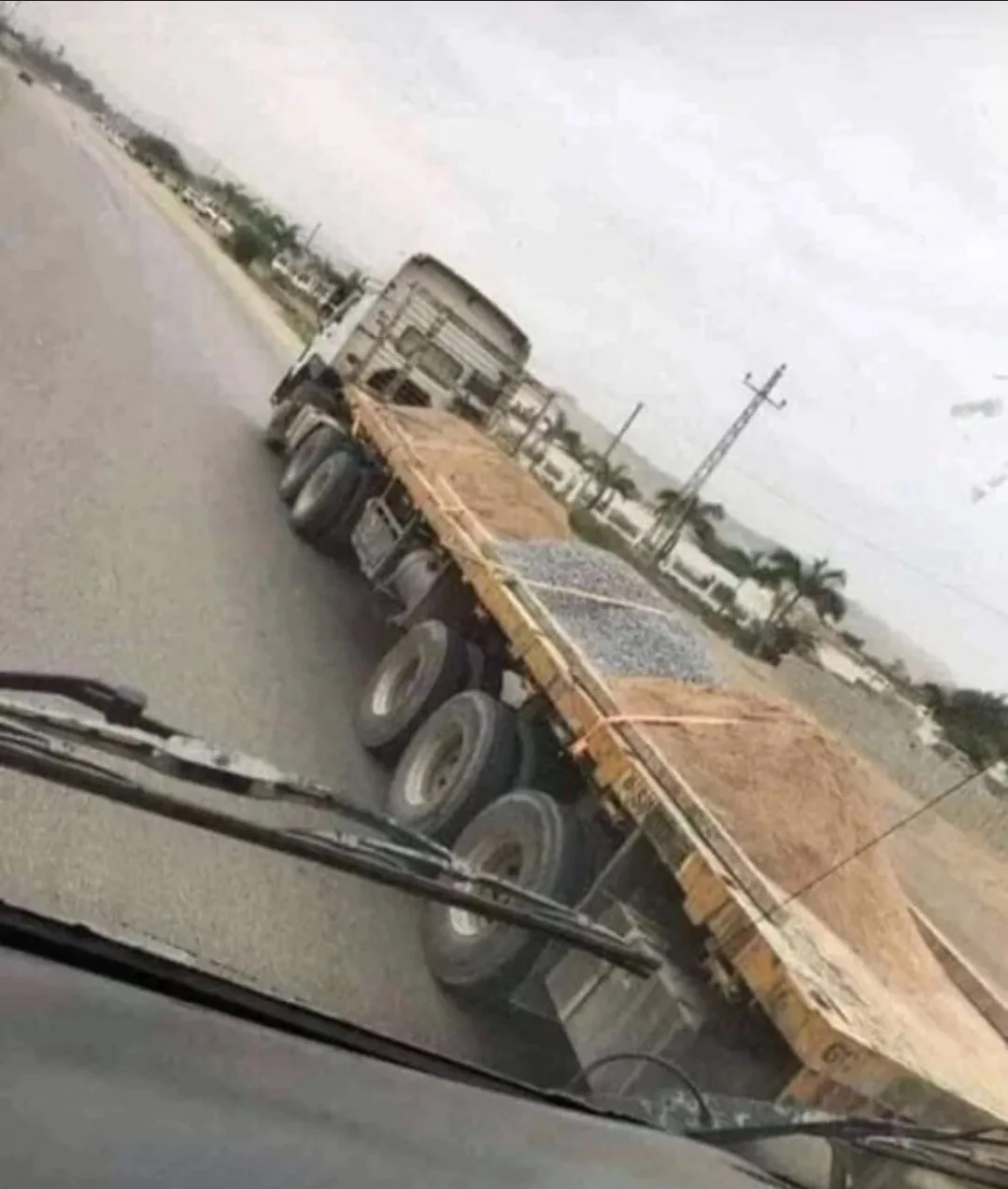 A blurry, tilted photo taken from inside a car shows a large flatbed truck driving on a road, viewed through the windshield…