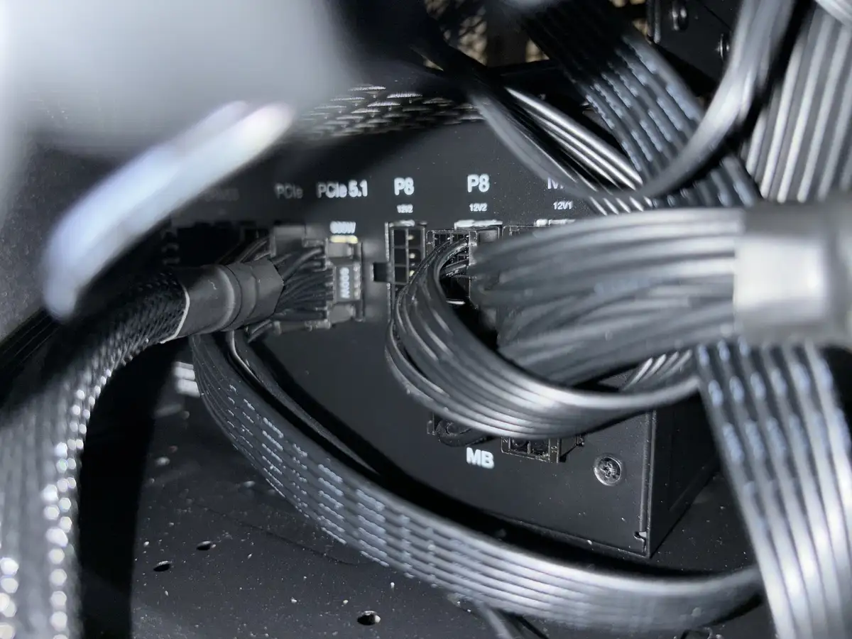 A close-up photo of a computer's power supply unit inside a case, showing multiple black cables plugged into labeled ports…