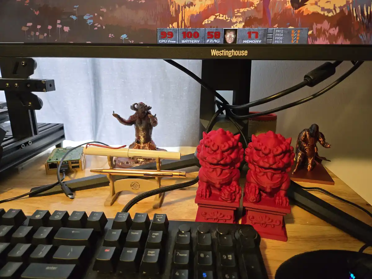 A desk setup with a Westinghouse monitor displaying a humorous fake game HUD with stats like '99 CPU FRAG', '100 BATTERY'…