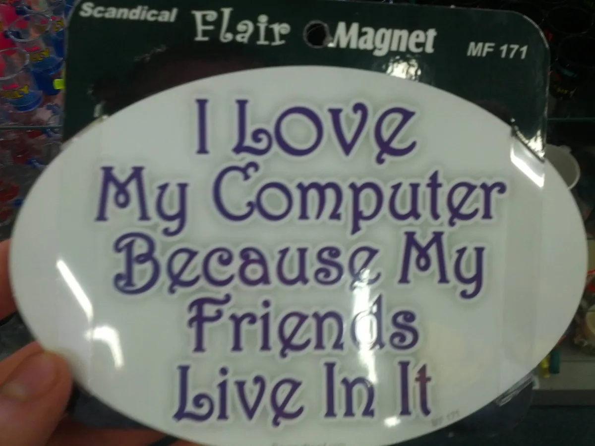 A person holds a white oval magnet with purple text that reads 'I Love My Computer Because My Friends Live In It'. The…