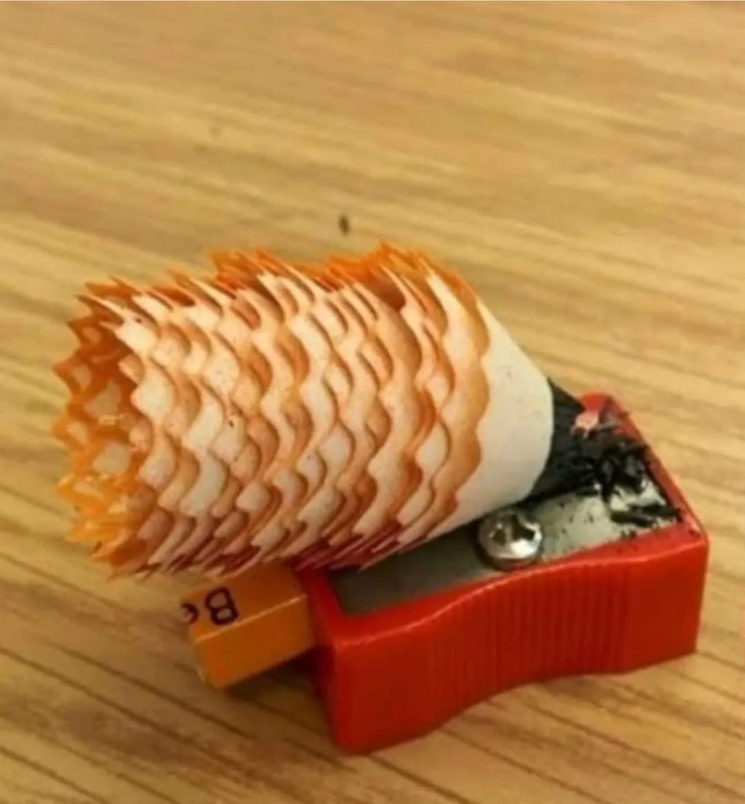 A pencil sharpener with a pencil inserted, but the pencil has been sharpened into a spiral of thin, orange-tipped shavings…
