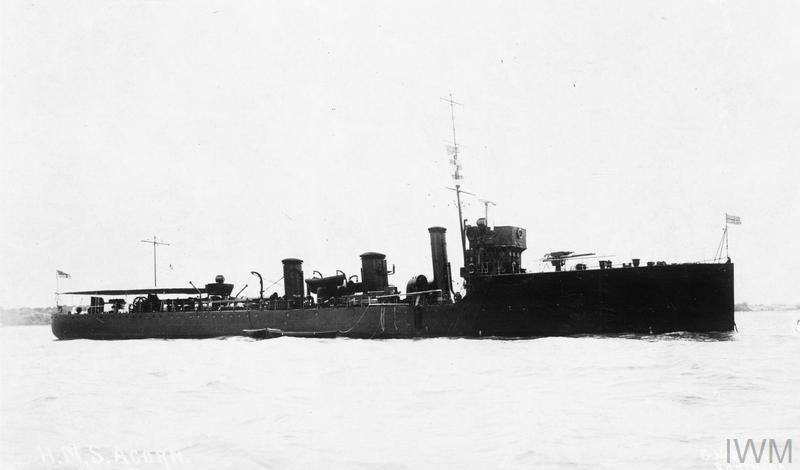 A black-and-white historical photograph shows a dark-hulled naval vessel, likely a destroyer or patrol boat, sailing on calm…