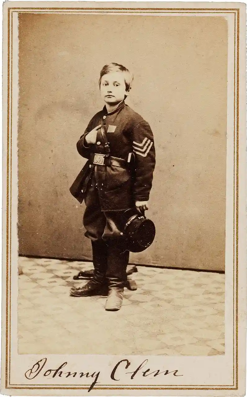 A vintage sepia-toned portrait of a young boy, identified as Johnny Clem, dressed in a Union Army uniform with sergeant…