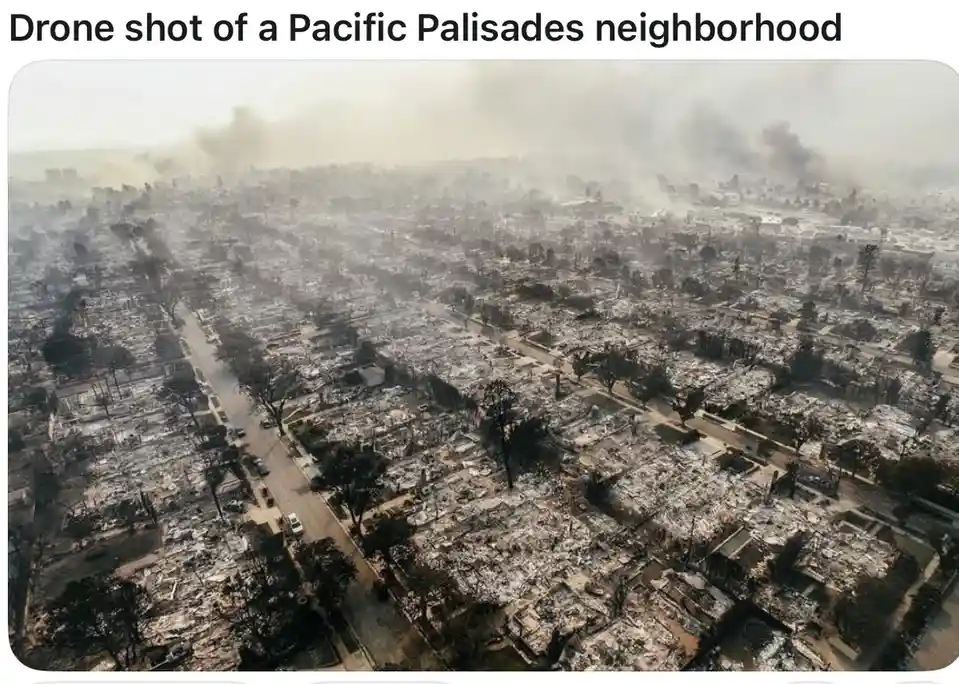 An aerial drone photograph shows a residential neighborhood in ruins, with most houses reduced to charred rubble and ash…
