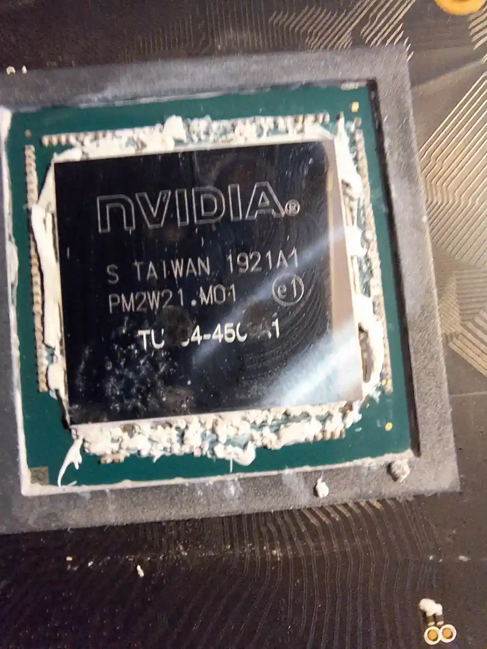 A close-up photo of a damaged NVIDIA graphics processing unit (GPU) chip, showing its printed markings and the melted…