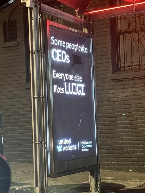 A nighttime photo of a digital billboard on a brick building, displaying white text on a dark background. The text reads…
