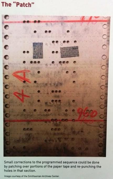 A close-up photograph of an old, worn paper tape with holes, showing two rectangular patches applied over sections of the…