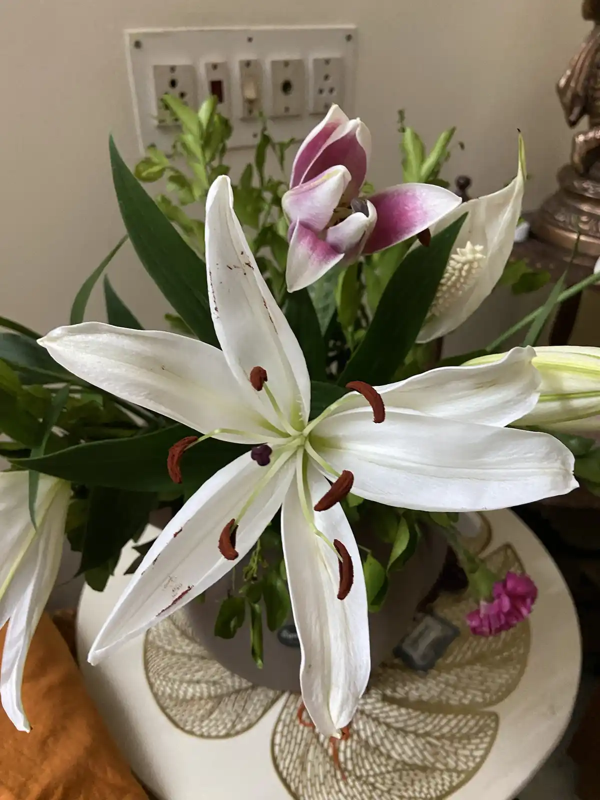A close-up photo of a bouquet of lilies in a decorative vase, featuring a prominent white lily with brown stamens and a…