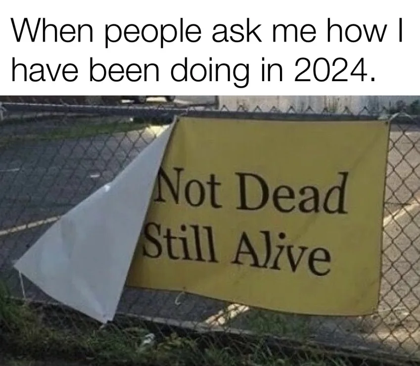 A yellow banner attached to a chain-link fence reads 'Not Dead Still Alive,' with a white triangular flag partially covering…