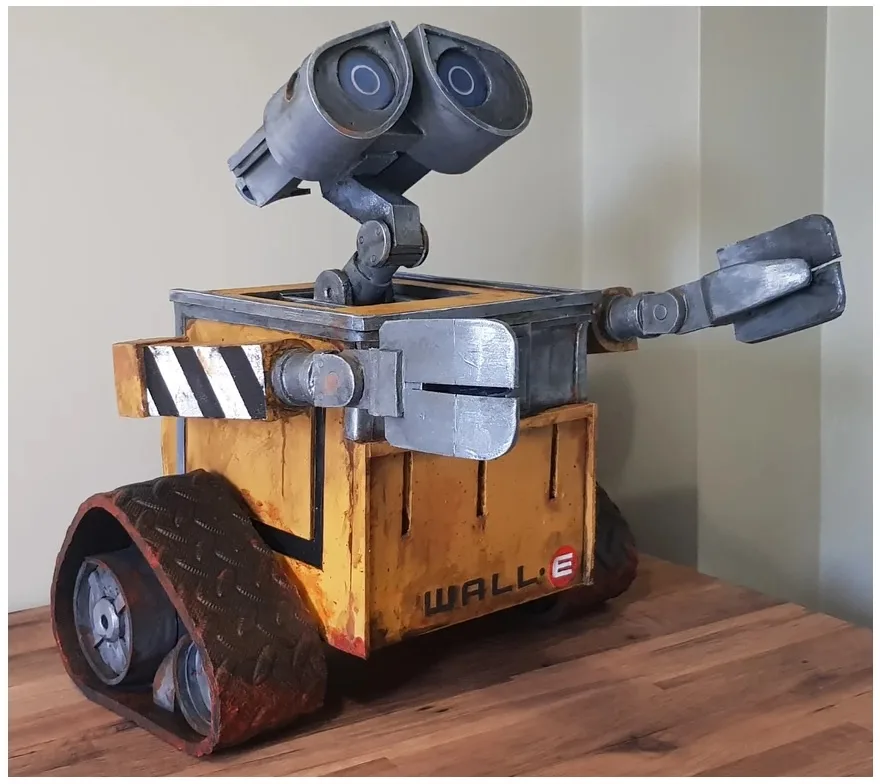 A handmade, detailed model of the robot WALL·E from the movie, standing on a wooden surface with its signature yellow body…