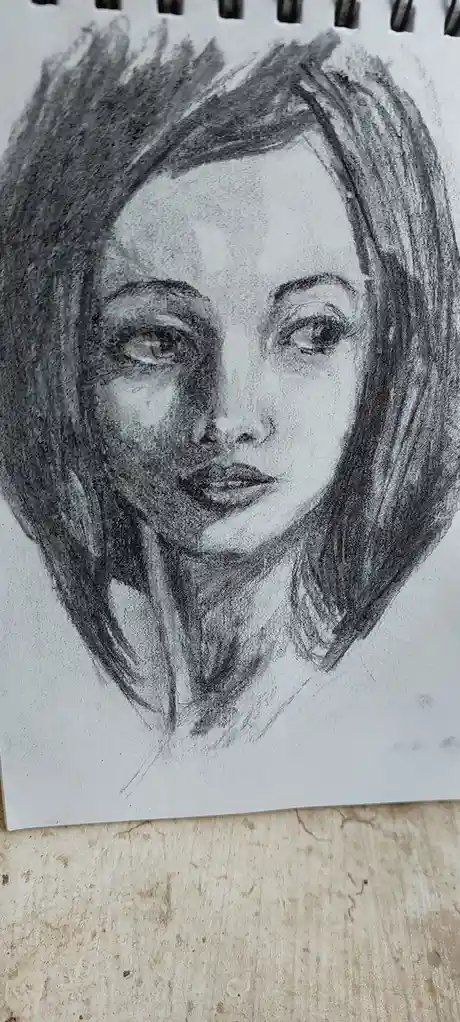 A detailed pencil sketch of a woman's face on a spiral-bound notebook page, showing expressive eyes, defined lips, and…
