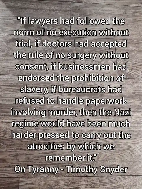 The image displays a block of white text with a black outline on a gray wooden floor background. The text is a quote from…