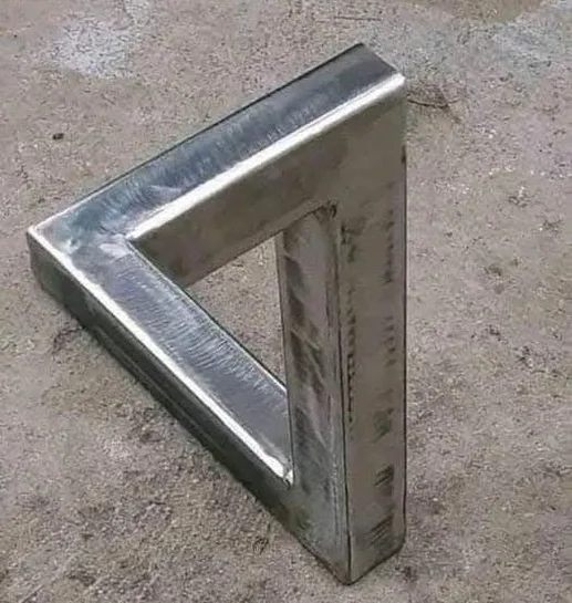 A metal object shaped like a triangle with three straight sides and three right angles, resting on a concrete floor. The…