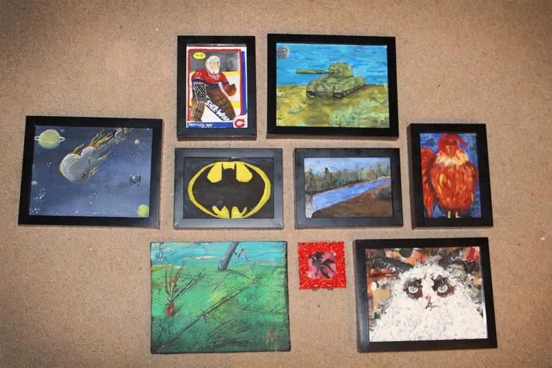 A collection of nine framed, childlike paintings displayed on a brown wall, depicting a hockey goalie, a tank, a comet, a…