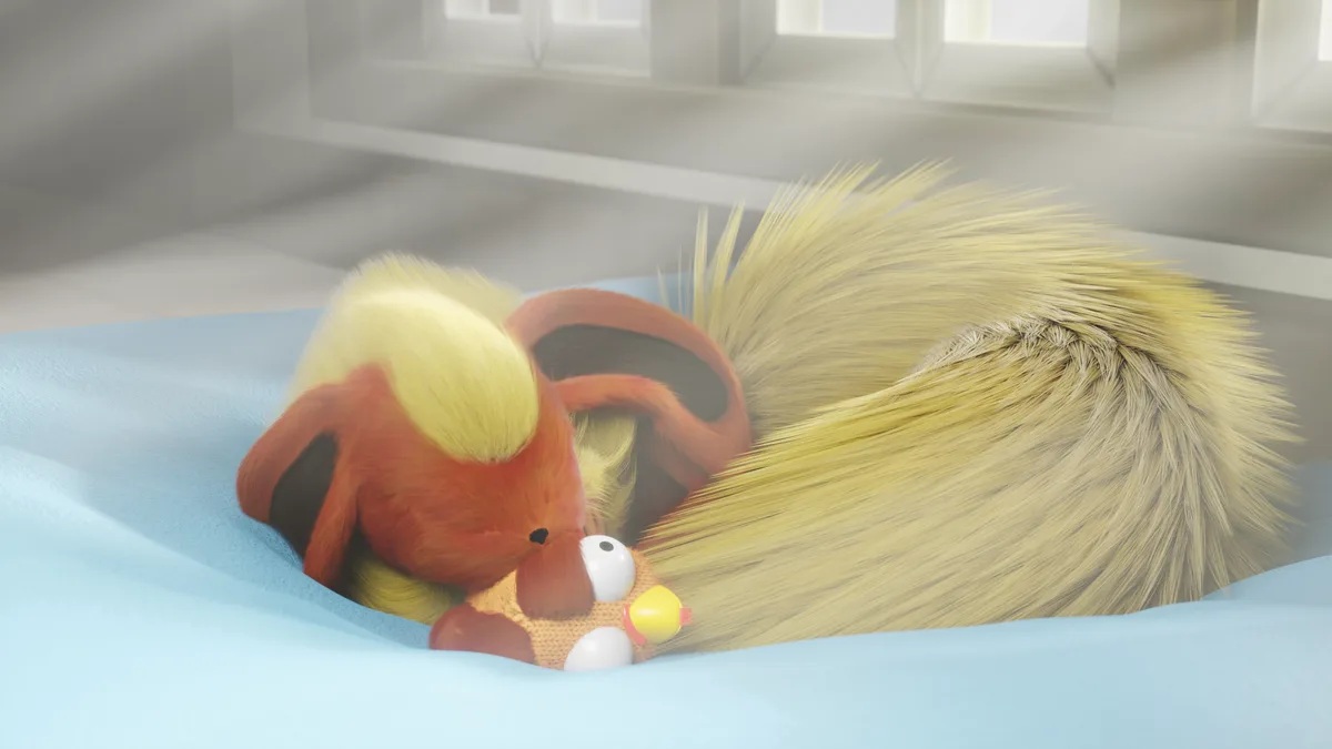 A fluffy, orange-and-yellow fox-like creature is curled up asleep on a light blue blanket, hugging a small knitted toy with…