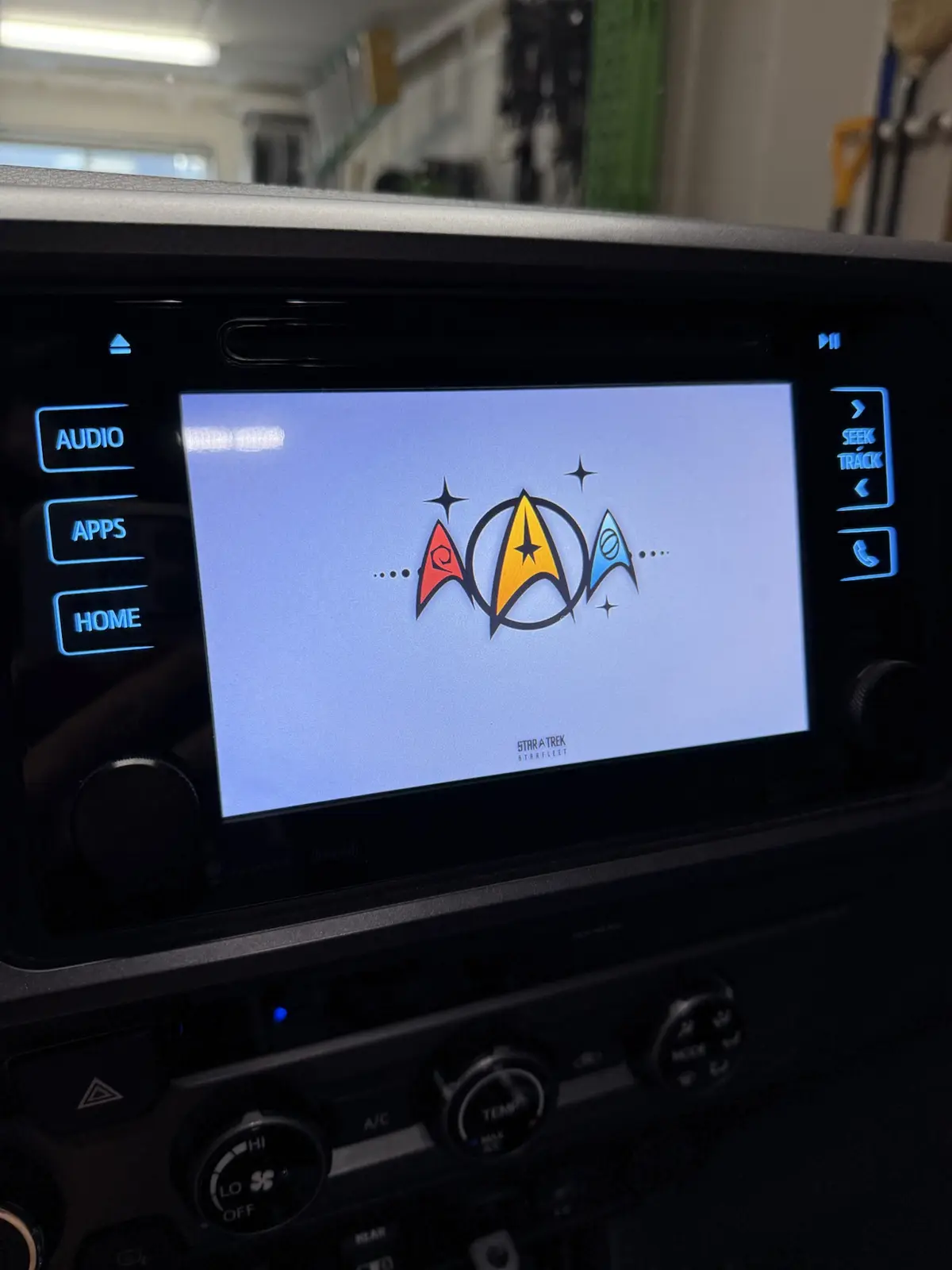 A close-up of a car's infotainment screen displaying the Star Trek Starfleet logo, which is creatively modified to resemble…