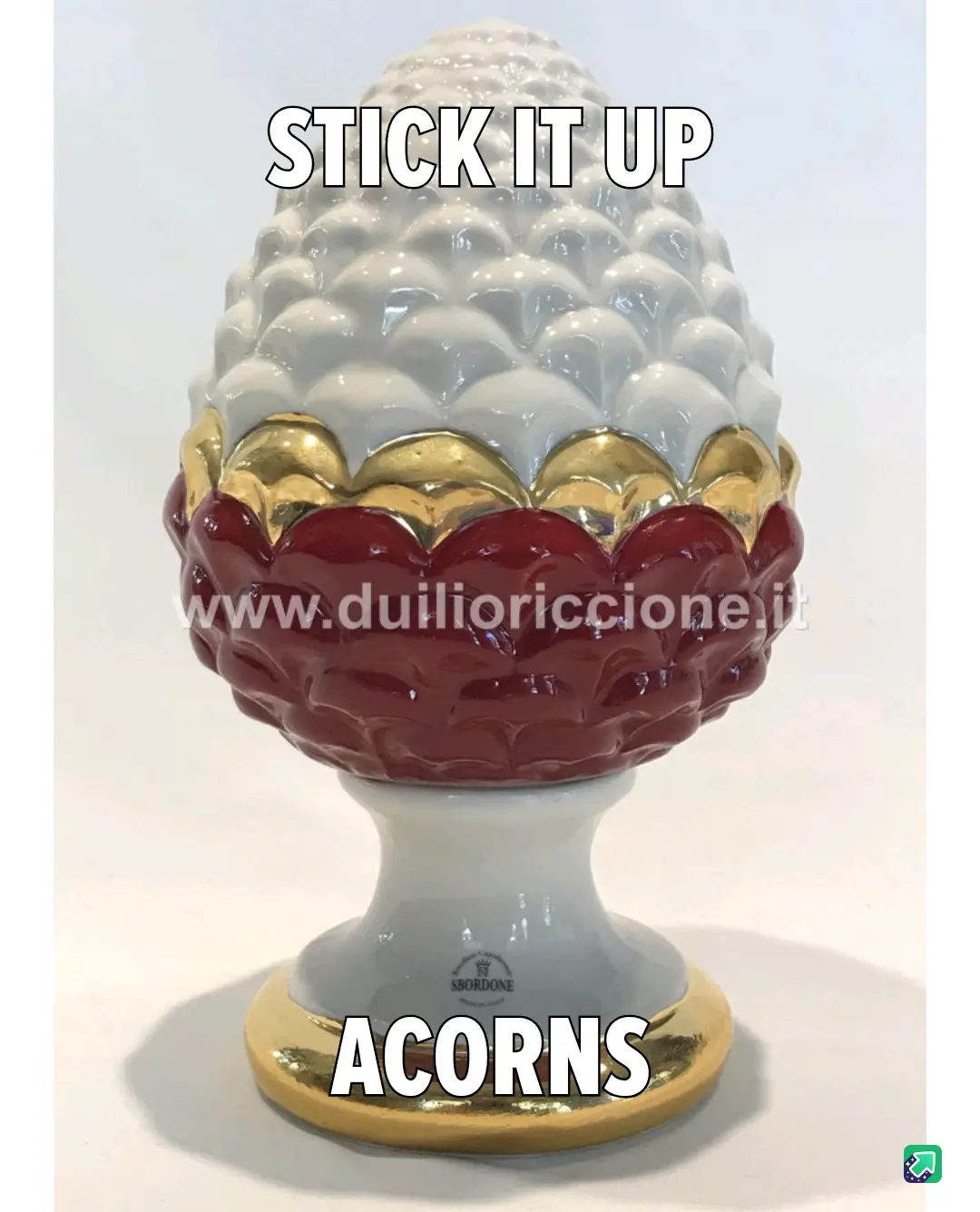 A ceramic decorative object shaped like a pinecone, with a white upper section, a gold middle band, and a red lower section…