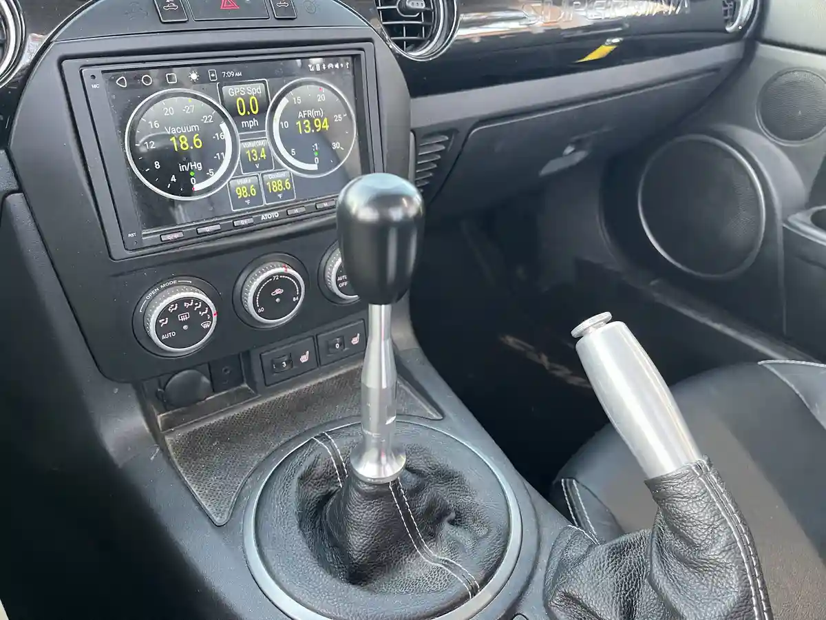 A close-up of a car's interior showing a manual gear shifter, a digital dashboard displaying engine metrics like vacuum and…