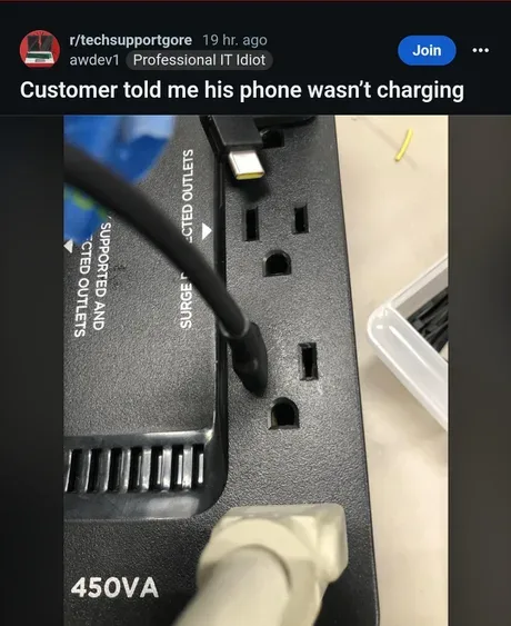 A close-up photo of a black surge protector with a USB-C cable plugged into one of its outlets, and a beige phone charger…