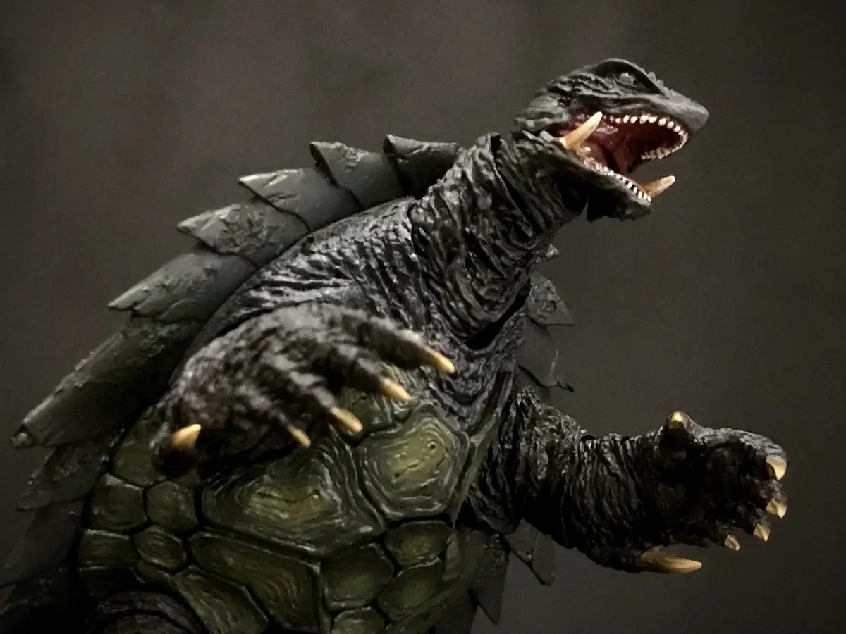 A detailed Godzilla action figure is shown with its mouth open and claws extended, but its back and belly are covered in…