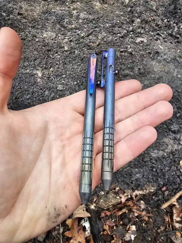 A person's open palm holds two identical-looking, dark metallic pens with iridescent clips and textured grips, set against a…