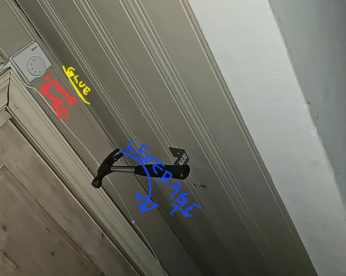 A close-up photo of a hammer wedged into a gap in a wall or door frame, with handwritten text annotations in red, yellow…