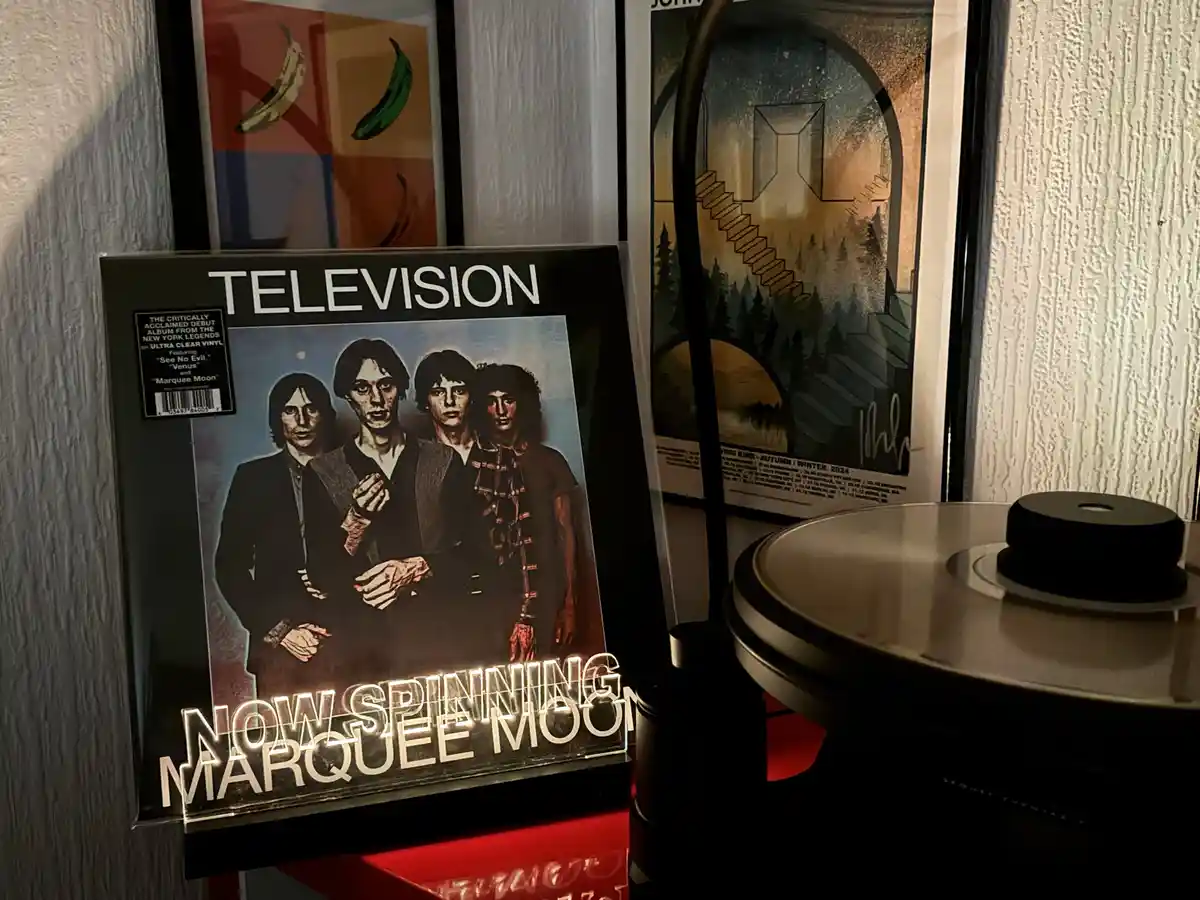 A vinyl record album cover for the band Television, featuring a photo of four band members, is displayed next to a…