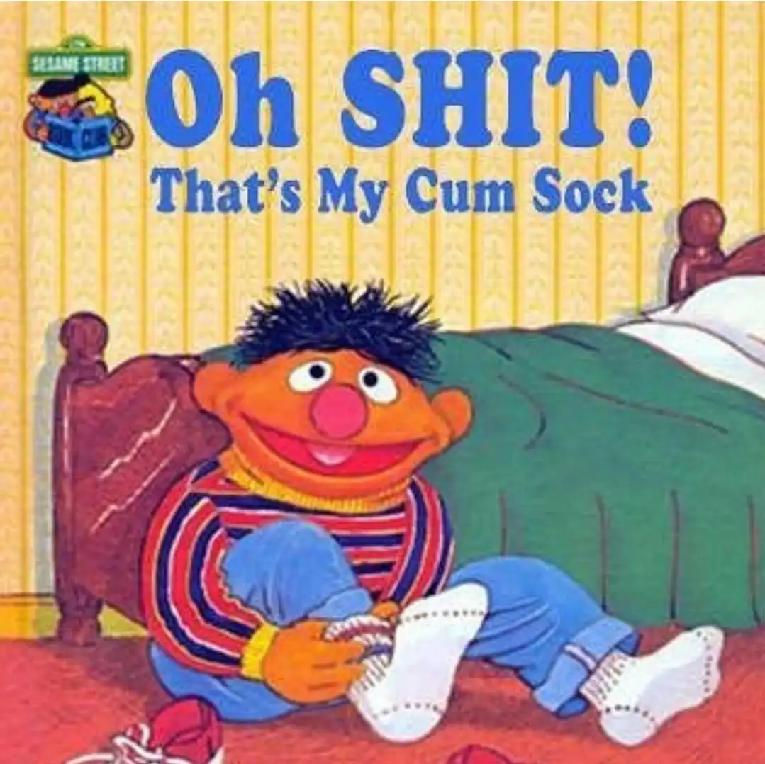The image shows the Sesame Street character Ernie sitting on a red floor in front of a bed, holding a white sock with a…
