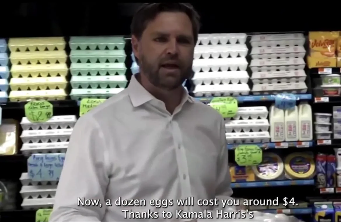 A man in a white shirt stands in a grocery store aisle filled with egg cartons and dairy products, with price tags visible…