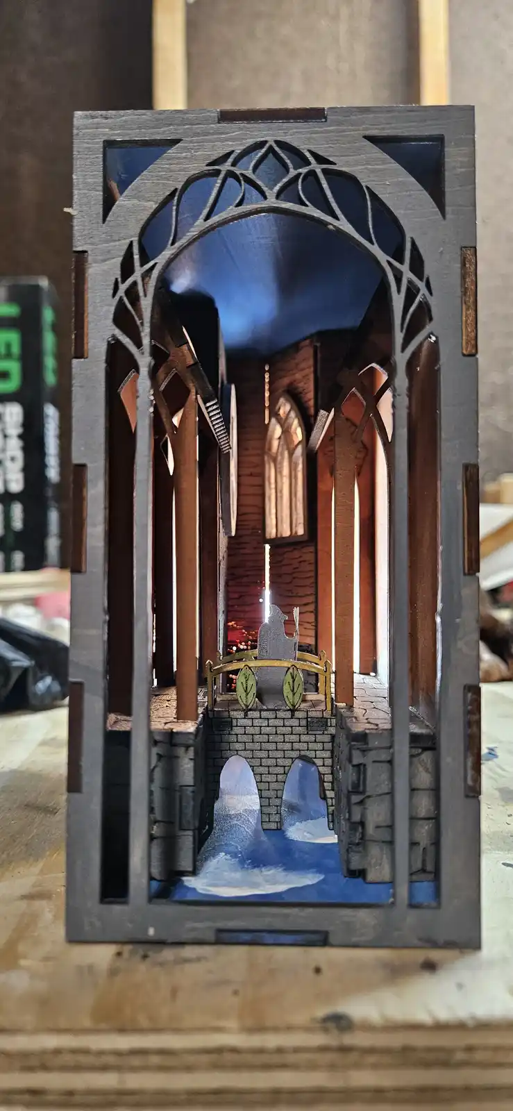 A handcrafted, layered wooden diorama depicts a miniature Gothic-style church interior with arched windows, brick walls, and…