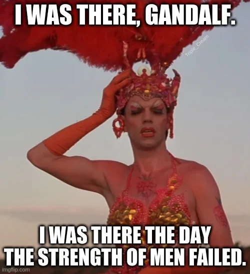 A person in a vibrant red and gold feathered costume with matching gloves and makeup, posing with one hand on their head…