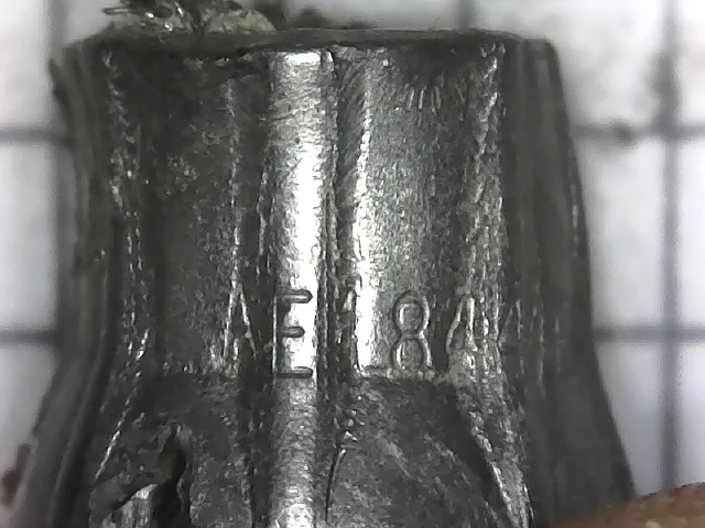 A close-up photo of a worn, metallic object with the stamped numbers 'E 84' visible on its surface. The object appears to be…