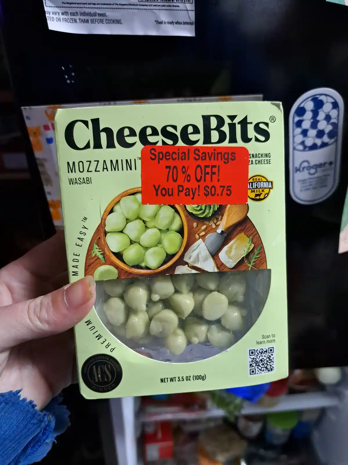 A hand holds a box of 'CheeseBits Mozzamini Wasabi' snack cheese, which has a red store sticker advertising 'Special Savings…