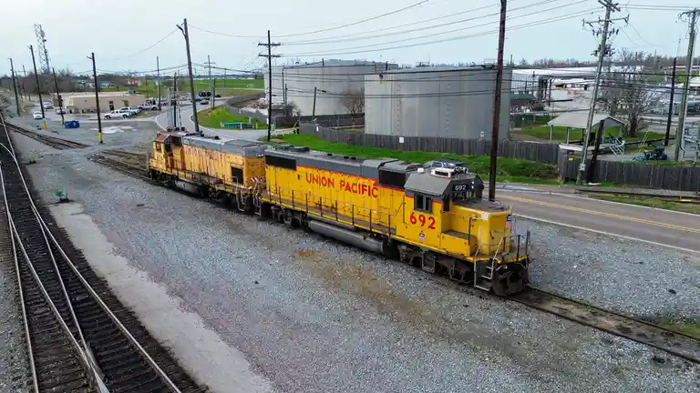 A yellow Union Pacific locomotive numbered 692 sits on railway tracks near industrial buildings and power lines. The image…