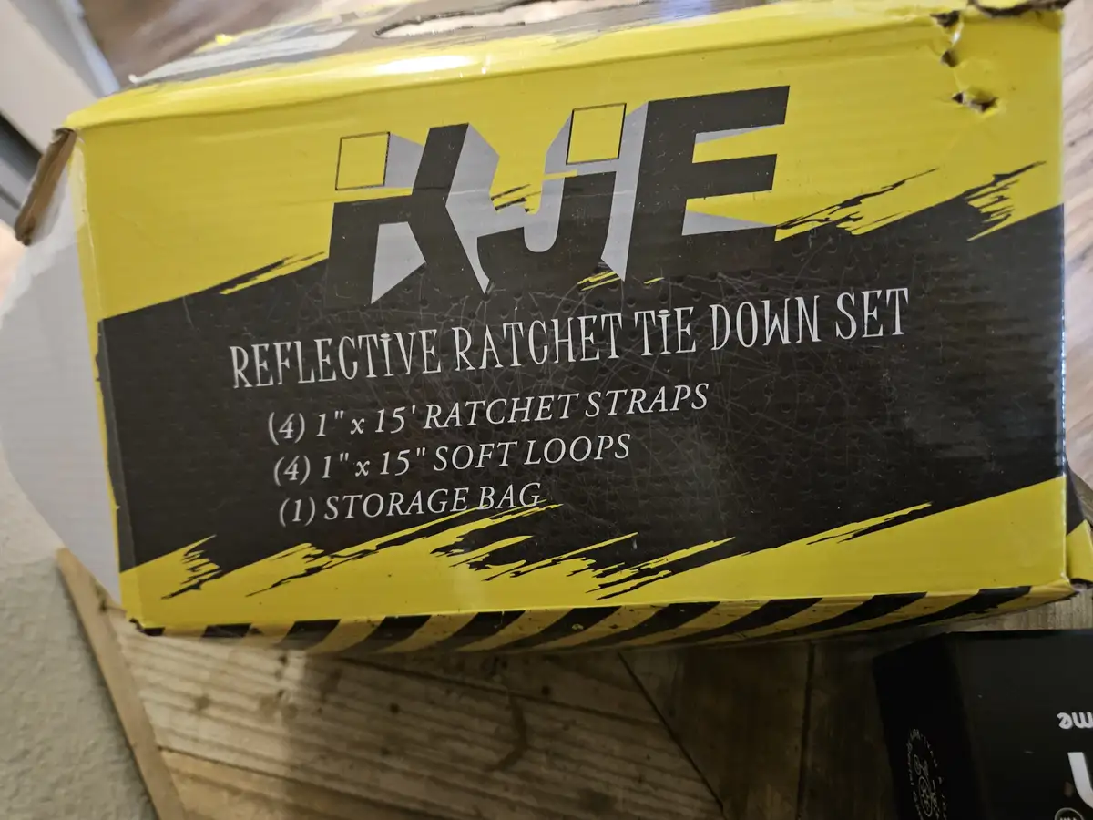 A close-up photo of a yellow and black box labeled 'KHE REFLECTIVE RATCHET TIE DOWN SET' with a list of contents including…