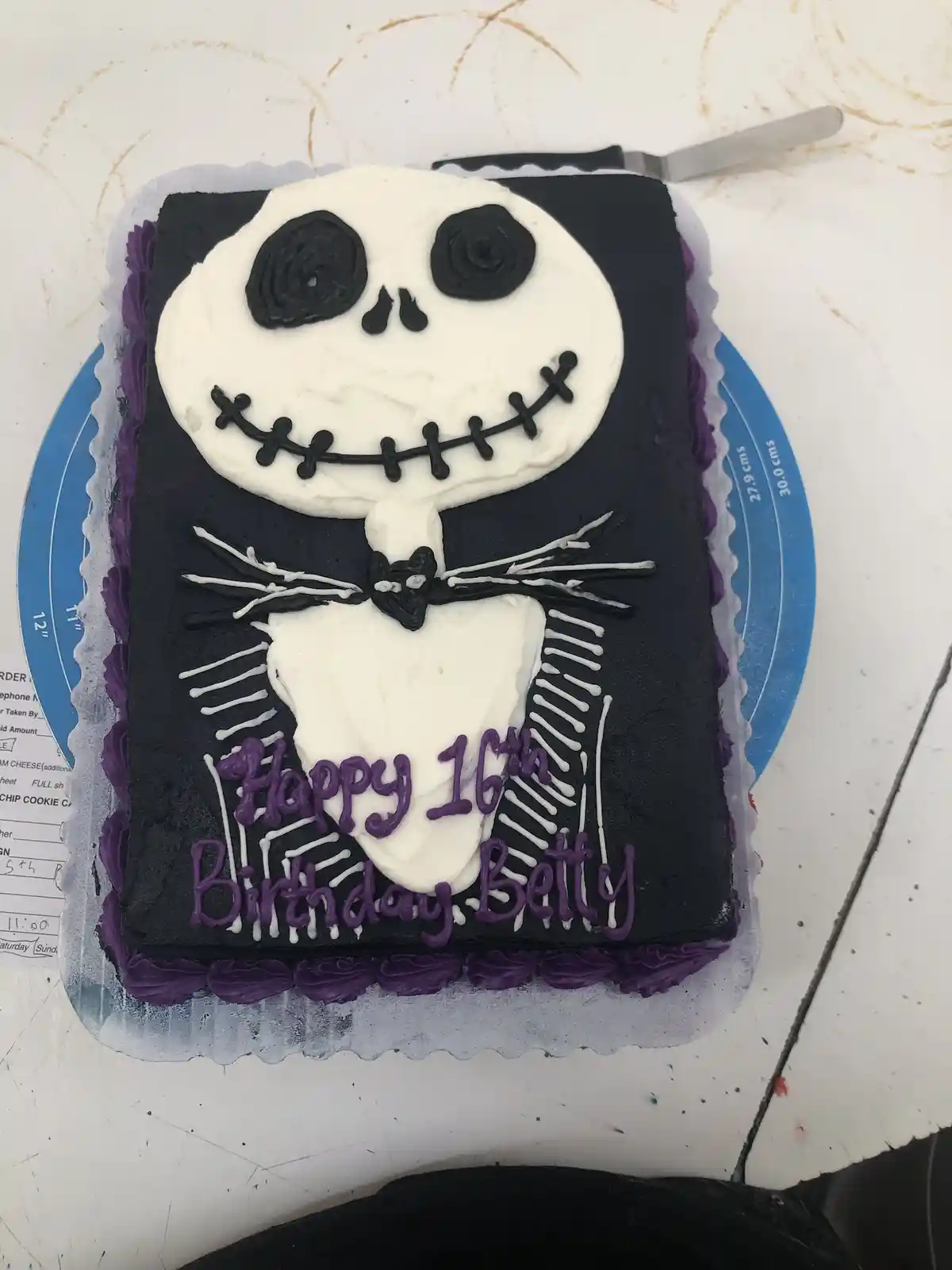 A rectangular birthday cake decorated to resemble Jack Skellington from The Nightmare Before Christmas, featuring white…
