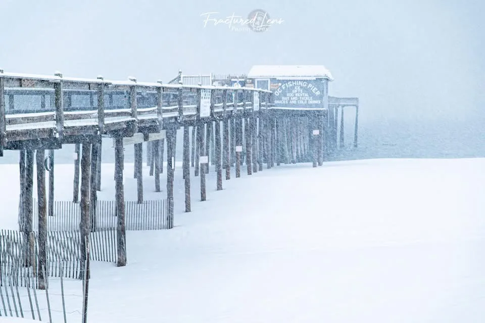 A wooden fishing pier covered in snow, with a sign reading 'DC FISHING PIER' and listing offerings like 'GIFT', 'ROD…