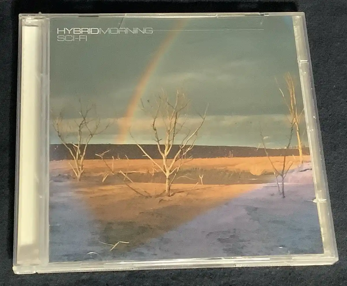 A CD case for 'Hybrid Morning Sci-Fi' shows a barren landscape with leafless trees under a cloudy sky, featuring a faint…