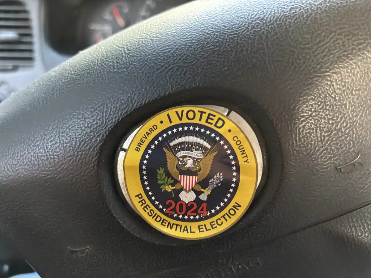 A close-up photo shows a 2024 'I VOTED' presidential election sticker from Brevard County, Florida, stuck on a black leather…
