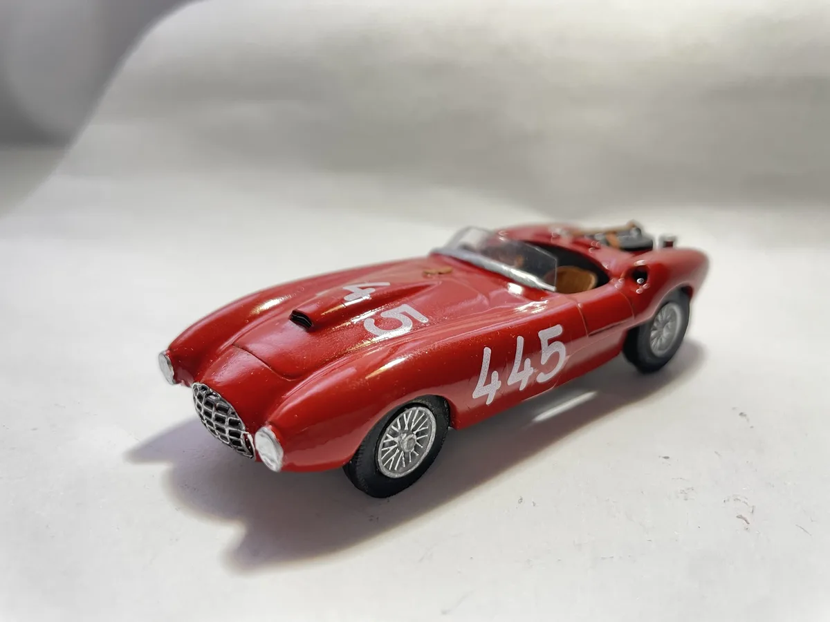 A red die-cast model of a vintage race car, likely a Ferrari, is shown on a plain white surface. The car has the number…
