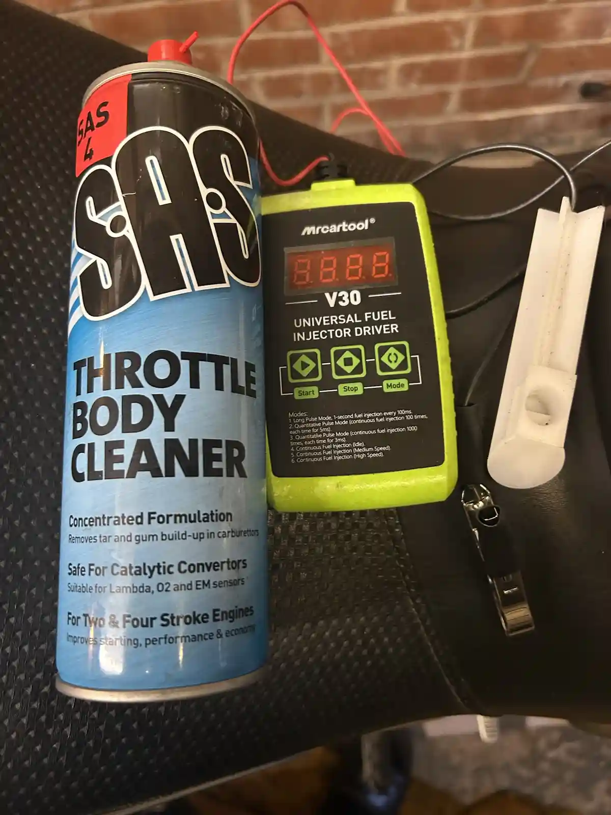 A can of SAS Throttle Body Cleaner sits next to a green 'Mrcartool V30 Universal Fuel Injector Driver' device displaying…