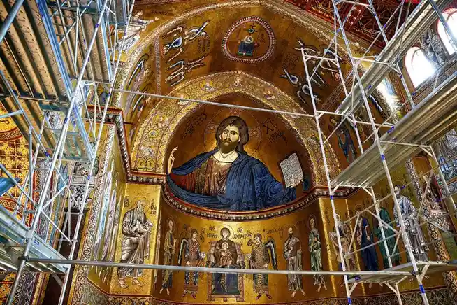 A grand, golden Byzantine mosaic of Jesus Christ holding a book is partially obscured by extensive metal scaffolding…