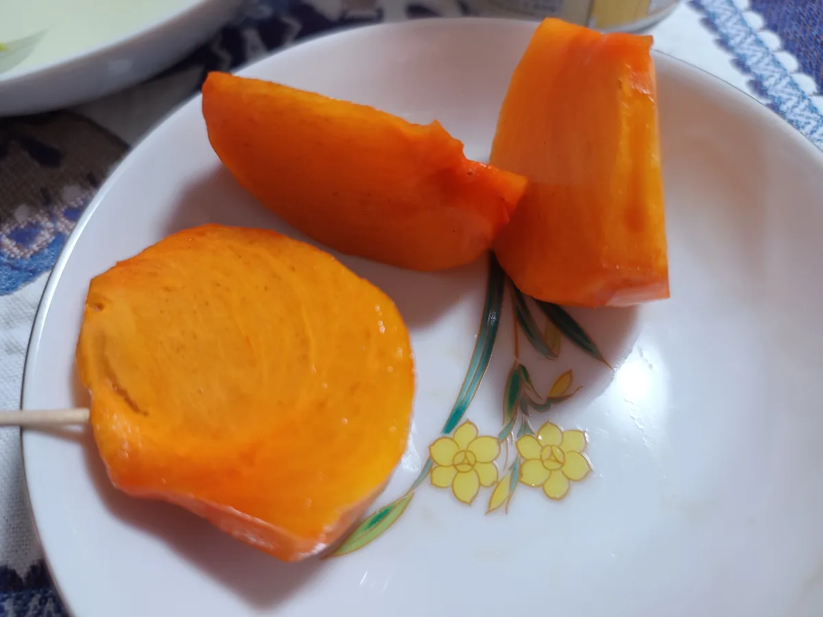 A white plate with a floral pattern holds three slices of bright orange papaya, one pierced with a wooden skewer. The…
