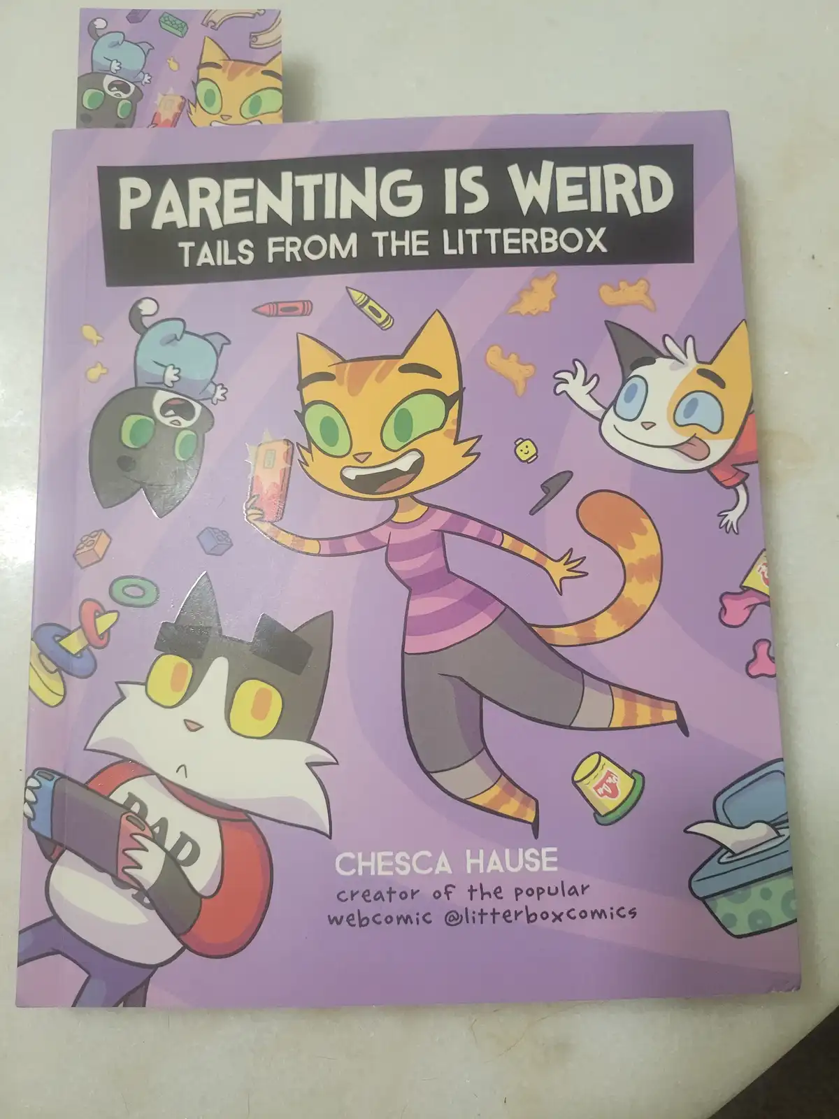 A book cover titled 'PARENTING IS WEIRD TAILS FROM THE LITTERBOX' by Chesca Hause, featuring cartoon cats in chaotic…