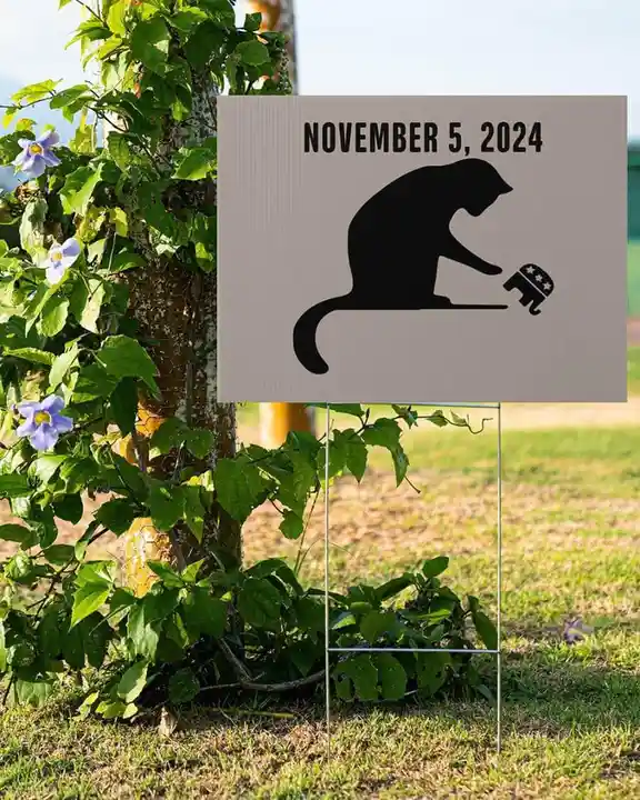 A yard sign with a black silhouette of a monkey sitting and peeling off a small elephant-shaped sticker. The sign is dated…