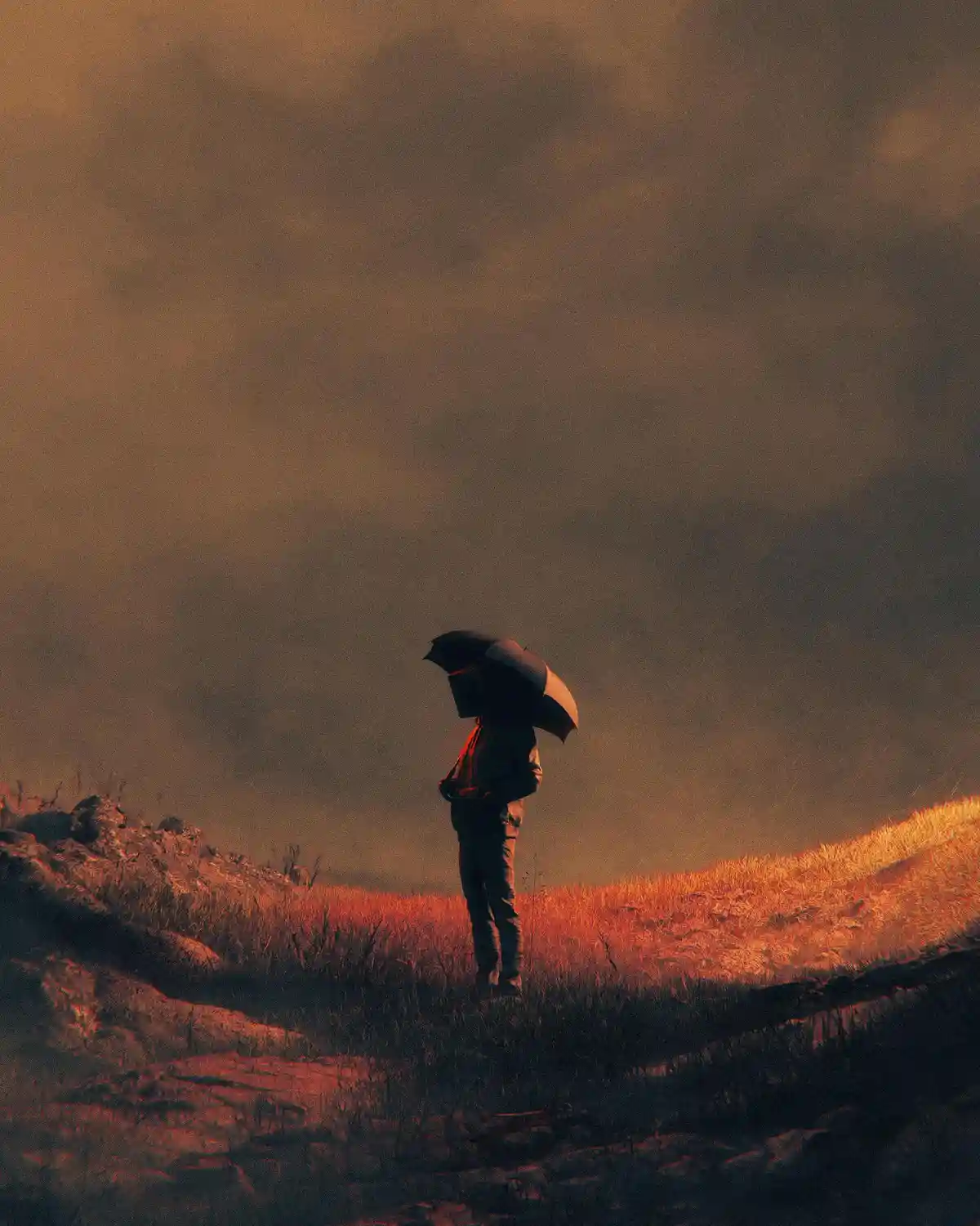 A solitary person stands in a field holding an open umbrella, silhouetted against a hazy, orange-tinted sky. The ground is…