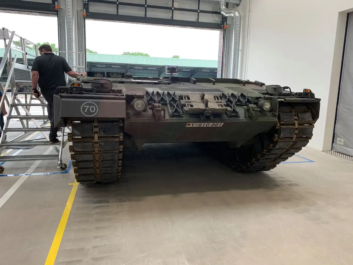A military armored vehicle, likely an infantry fighting vehicle, is parked inside a hangar with its rear facing the viewer…
